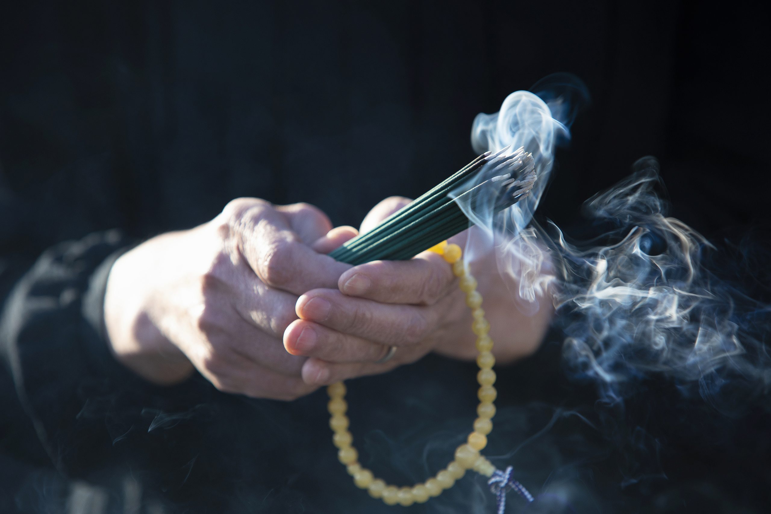 A funeral in Japan and a visit to a grave. Senior women have beads and incense sticks wearing black mourning. Smoke comes out from the incense stick.